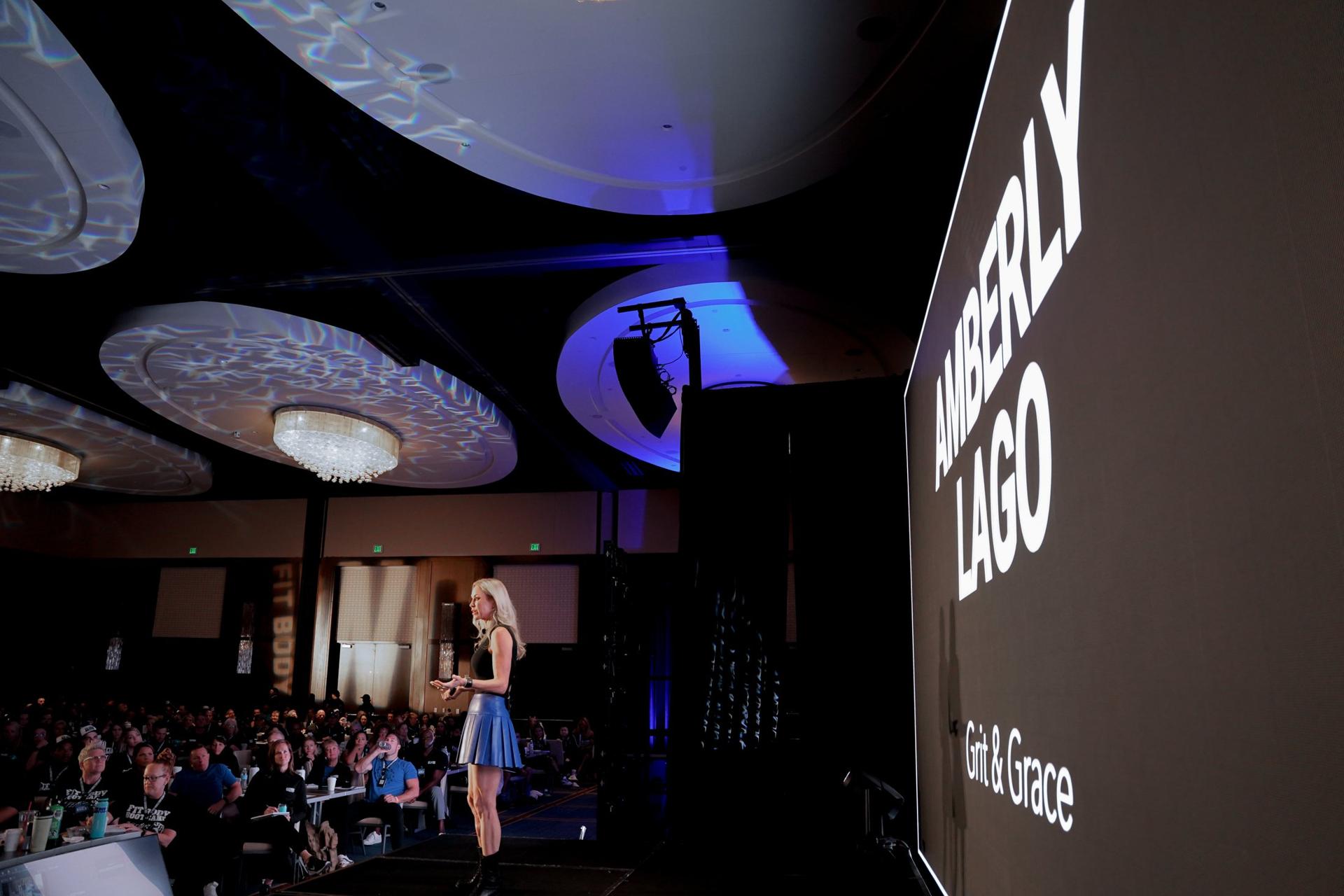 Amberly Lago speaking on stage, her name in lights